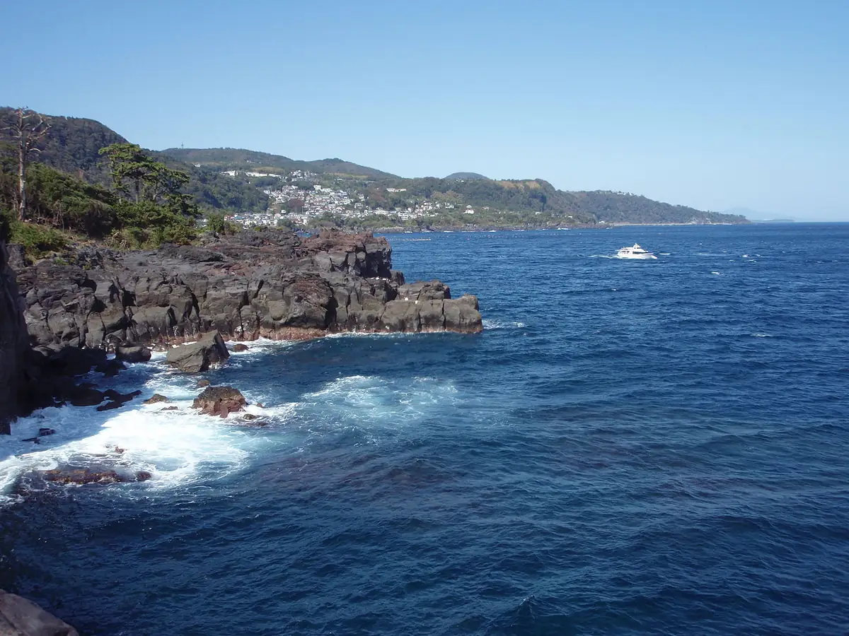 伊東市の城ヶ崎海岸。黒い溶岩の崖と青い海、白い波が続く実景。